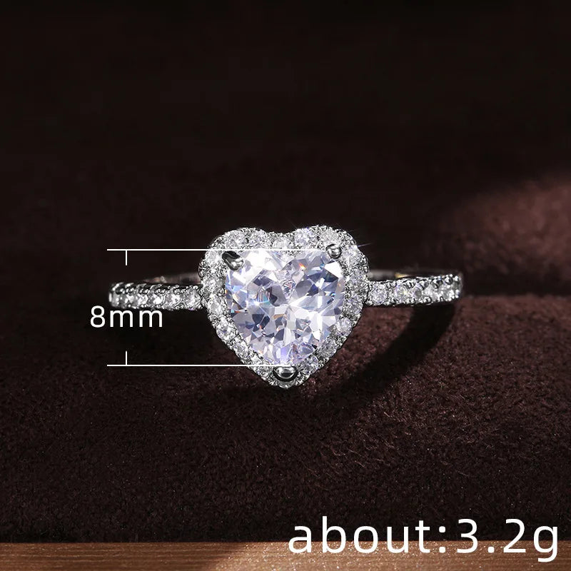 A close-up of a heart-shaped diamond ring with pave-set stones, measuring 8mm, resting on a dark surface.