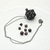 A set of metal polyhedral dice, including a d10, displayed next to a chain with a pendant storage case.
