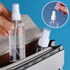 A hand is holding a clear refillable travel spray bottle with a fine mist pump, placed inside a leather-trimmed pouch.