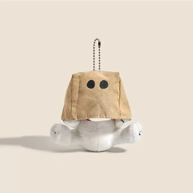 A tan plush charm shaped like a head with two black dots, attached to a chain, resting on a white fluffy object.