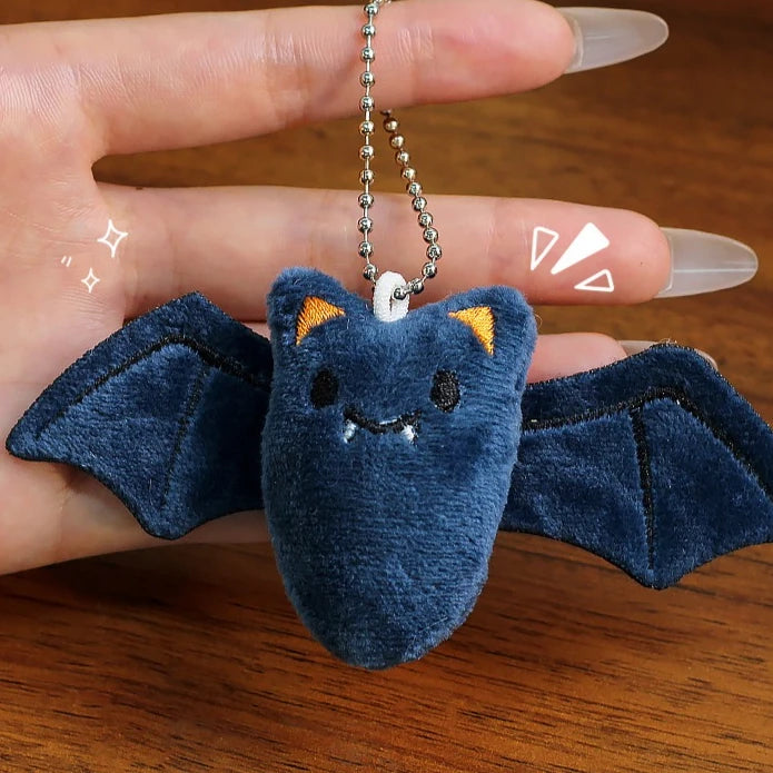 A dark blue plush keychain set featuring a ghost, pumpkin, and bat charm hanging from a silver chain.