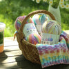 A woven basket filled with three balls of gradient acrylic yarn in various colors, resting on a wooden surface.