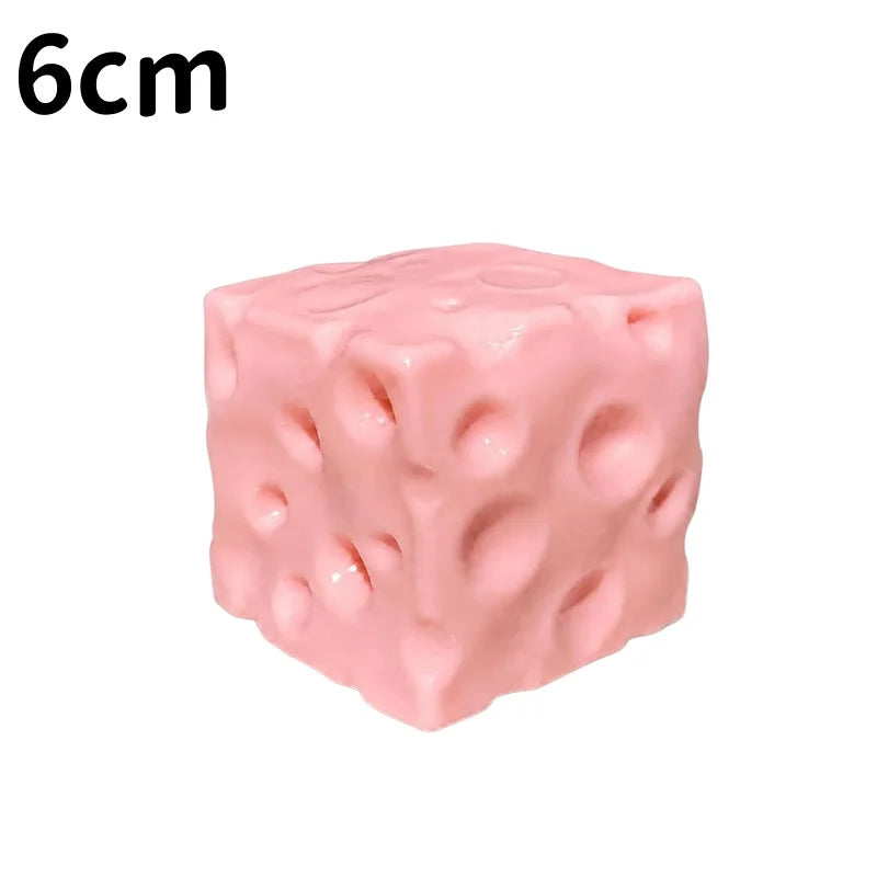 A pink, squishy cheese cube stress ball with a porous texture.
