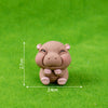A small, light brown resin figurine of a hippo with its paws together, photographed on green grass.