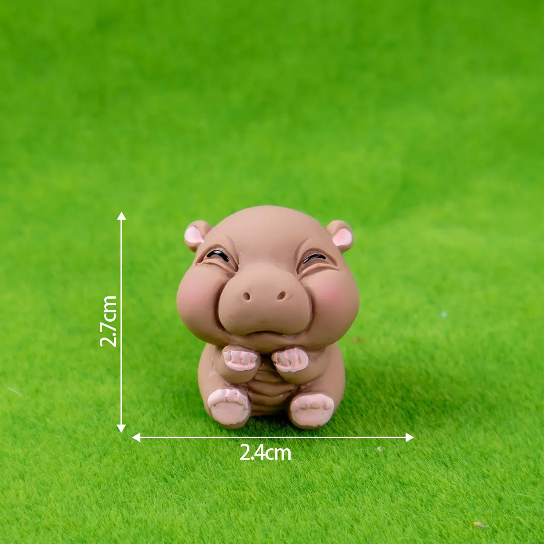A small, light brown resin figurine of a hippo with its paws together, photographed on green grass.