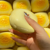 A hand holds a yellow squishy milk bread stress relief toy surrounded by similar yellow items.
