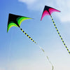 A large delta kite with a black and green canopy and a yellow and black striped tail flying against a blue sky.