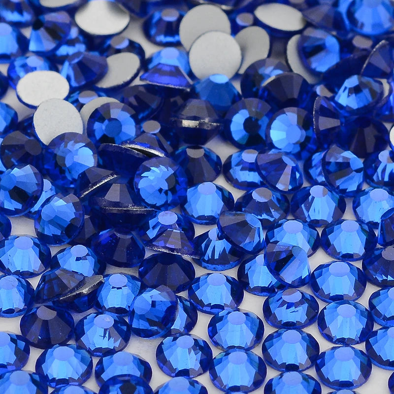 A close-up view of numerous brilliant blue and clear glass crystal flatback rhinestones scattered on a white surface.