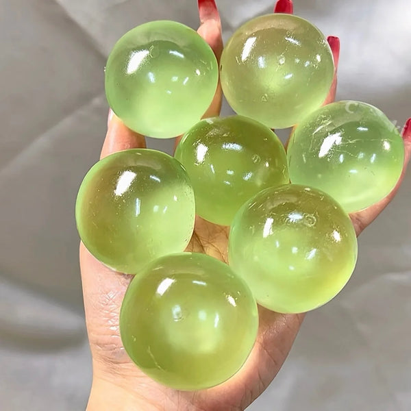 Une main tient plusieurs boules de stress en huile de coco translucide vert clair.
