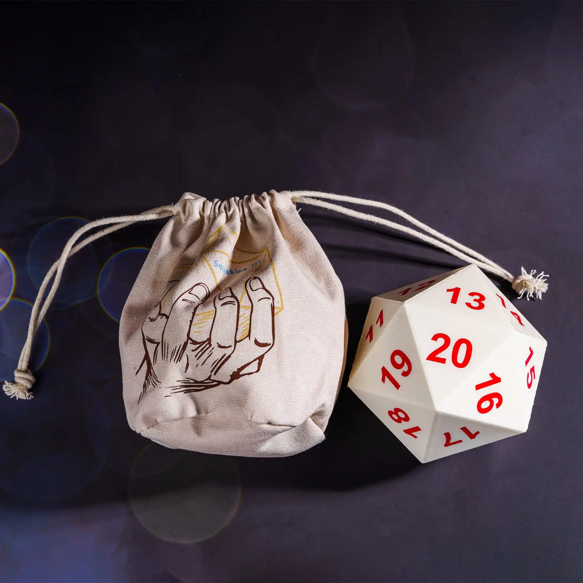 A beige drawstring bag with a handprint design and a white D20 polyhedral dice set resting on a dark surface.