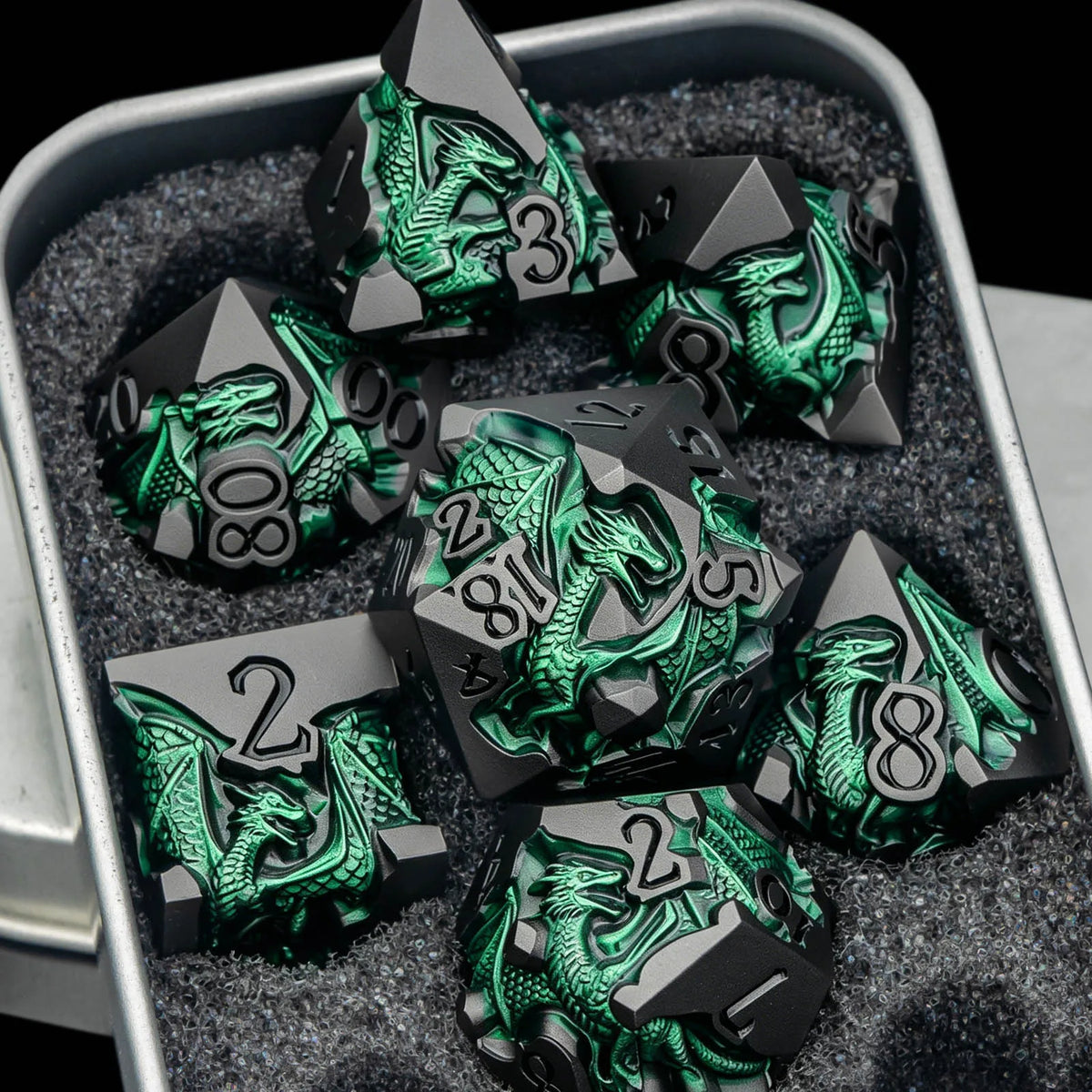 A set of black metal dice featuring a green dragon design resting in a dark gray, textured container.