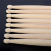 A set of five light-colored maple wood drumsticks arranged in a row against a dark background.