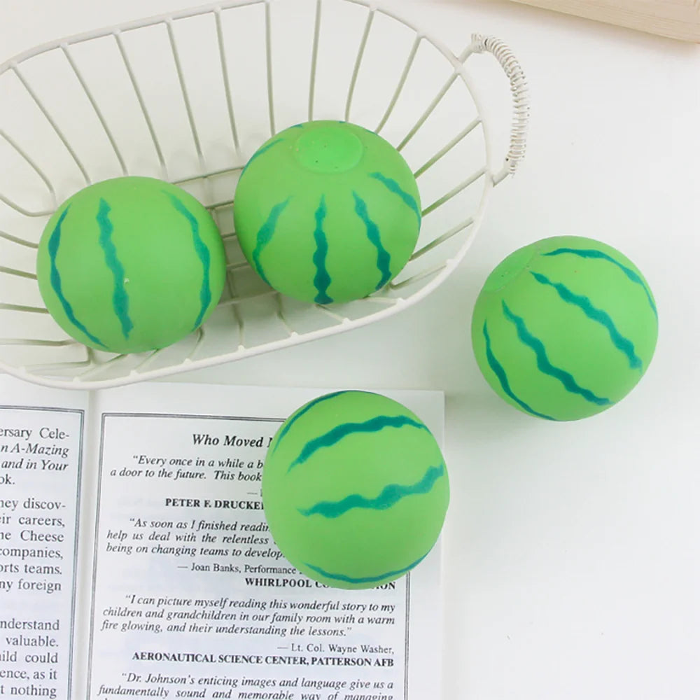 Grüner Wassermelonen-Stressball im weißen Drahtkorb neben einem Buch.