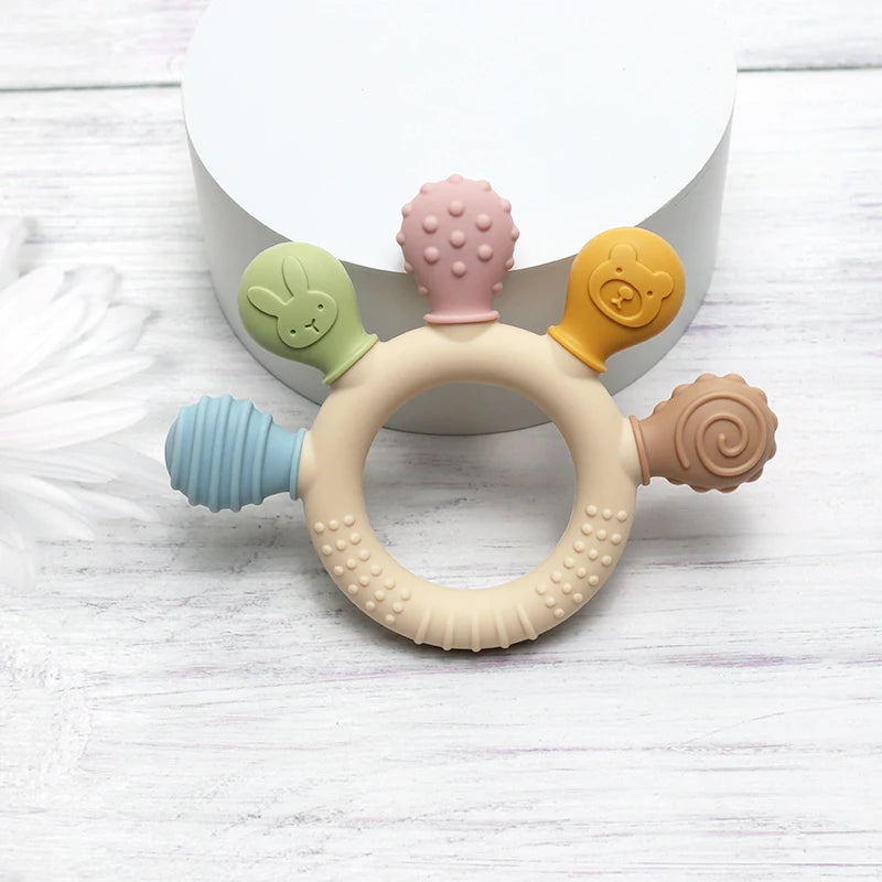 Set aus silikonigen Baby-Teethers in Pastellfarben, einschließlich rosa, grün und gelb, auf weißem Hintergrund.