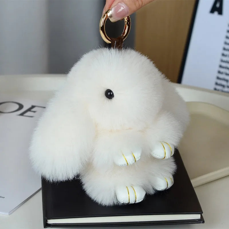 A fluffy white plush bunny keychain is being held by a hand, resting on a black book.