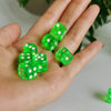 A hand holds several bright green transparent dice with white polka dots.