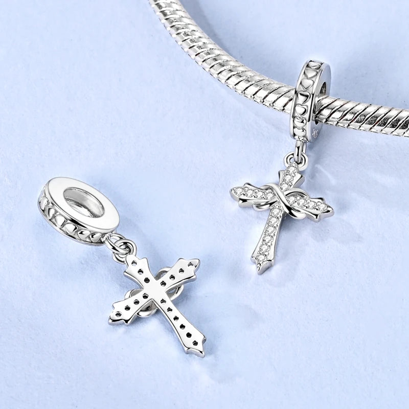 A sterling silver cross pendant and chain with charm beads shown against a light blue background.