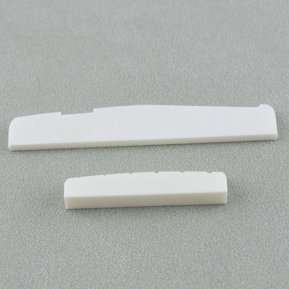 Two white guitar nut and bridge saddle components lying on a gray surface