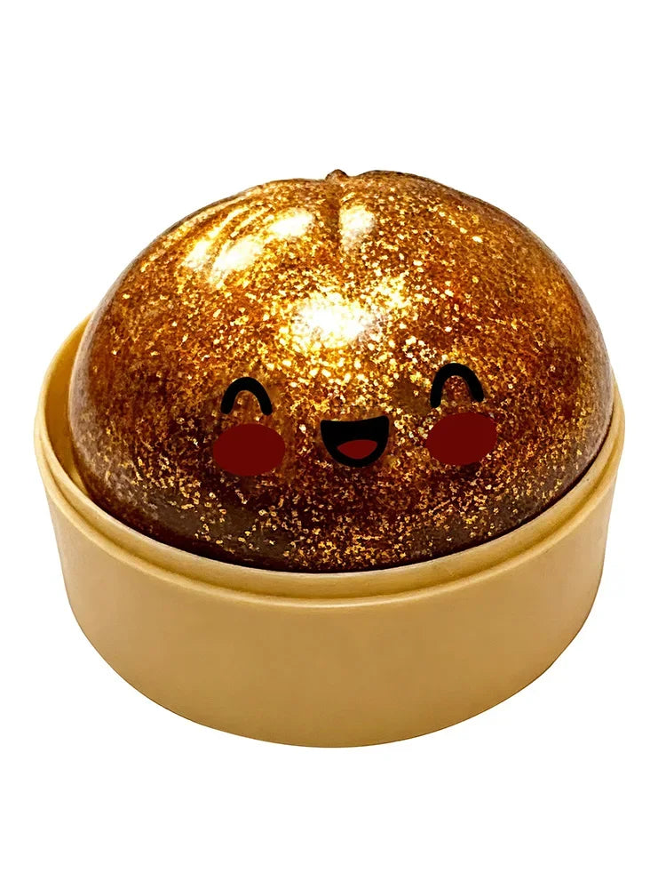A sparkling, round squishy toy resembling a face with cute eyes and a smile, resting in a light yellow container.