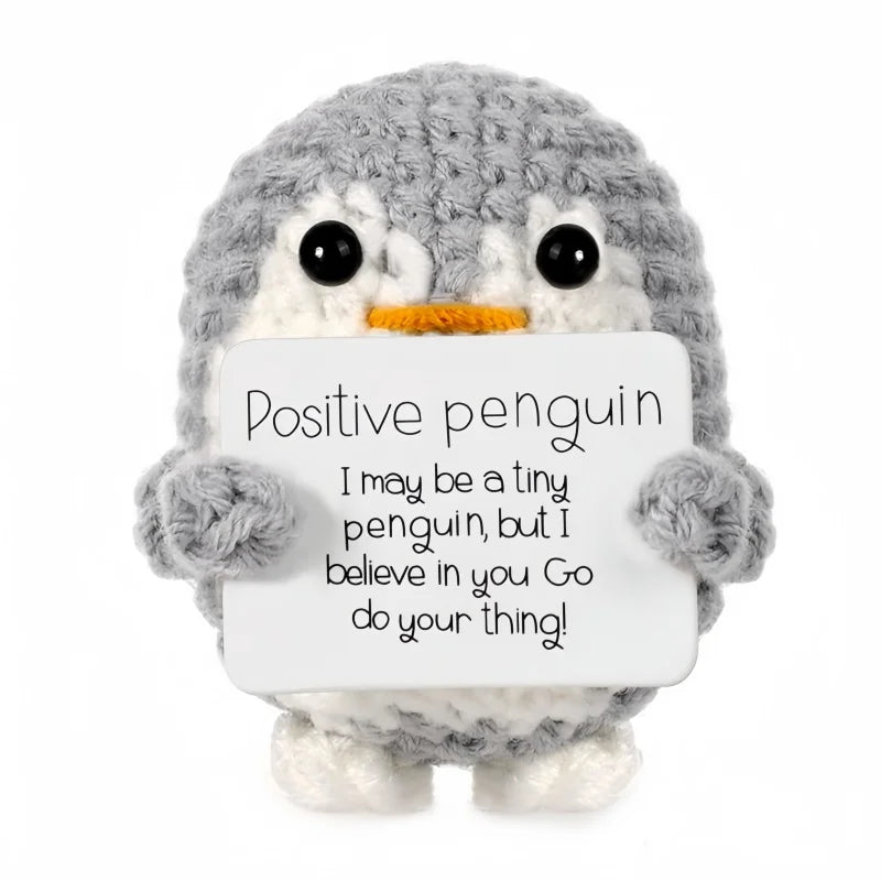 A handmade gray crochet penguin doll holding a card that says Positive penguin I may be a tiny penguin but I believe in you G