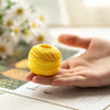 A hand holds a ball of bright yellow cotton crochet thread on a piece of paper.