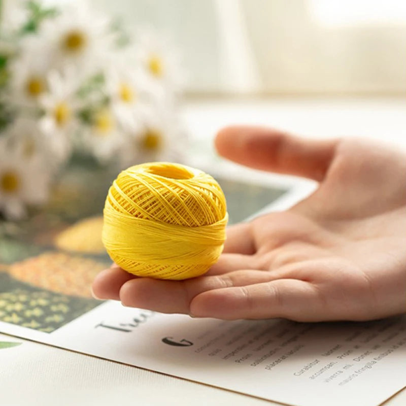 A hand holds a ball of bright yellow cotton crochet thread on a piece of paper.
