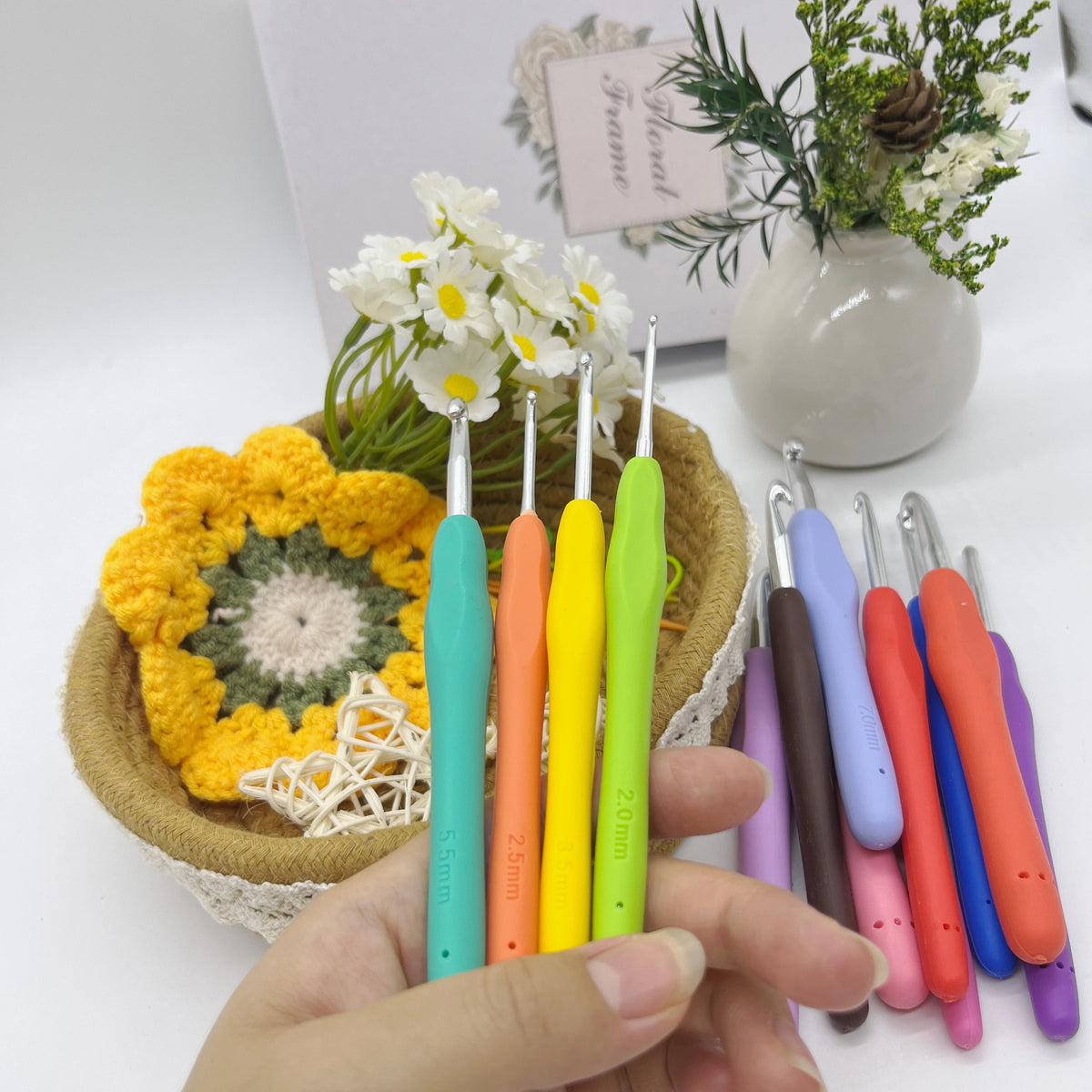 A hand holds an ergonomic crochet hook set with stitch markers and needles, featuring various colors like green, orange, and 