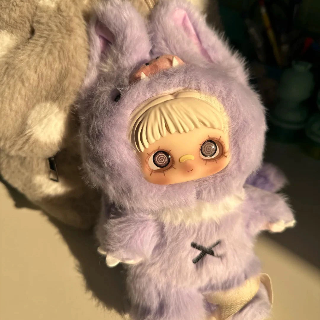 A purple fluffy plush doll with large ears and a facial feature resembling a baby face is shown.