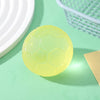 A round, translucent yellow football-shaped squishy fidget toy resting on a light green surface next to a white basket.