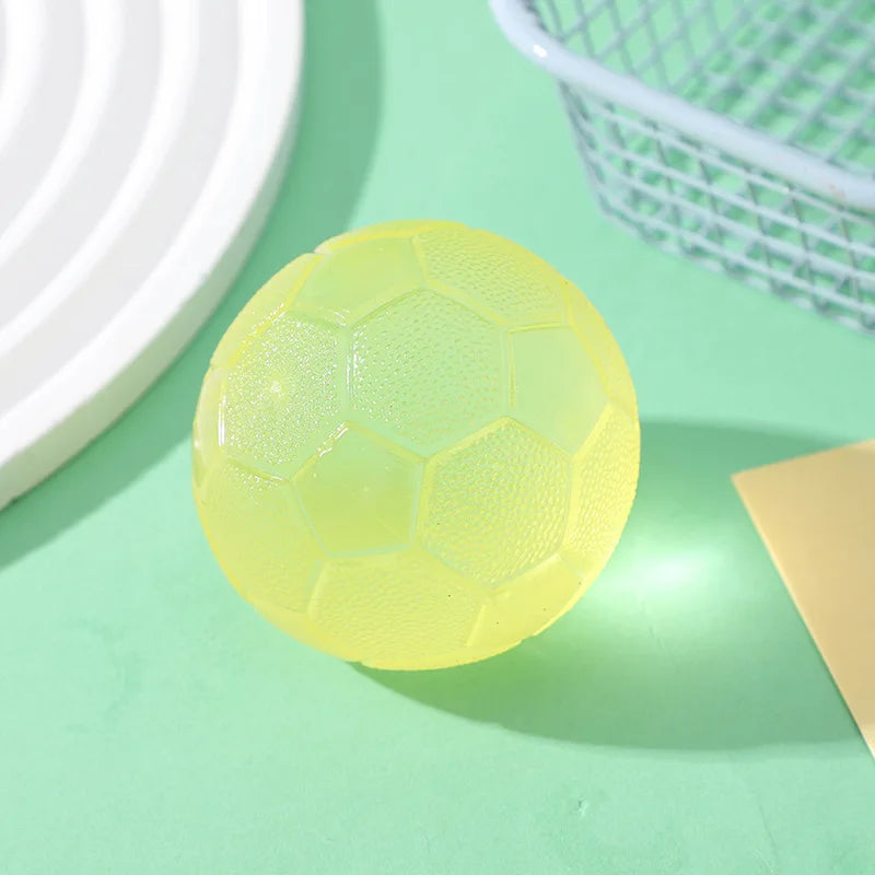 A round, translucent yellow football-shaped squishy fidget toy resting on a light green surface next to a white basket.