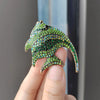 A hand holds a green rhinestone turtle brooch pin with iridescent stones against a blurred background.