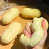 A hand is squeezing a yellow peanut butter squishy stress ball, with several other similar toys visible on a wooden plate.