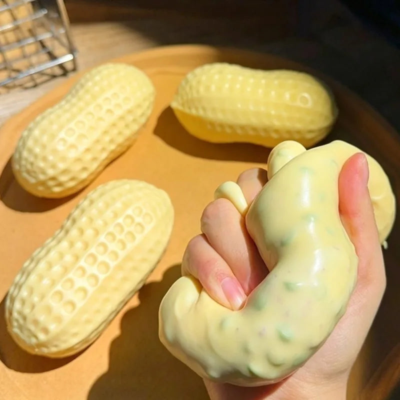 A hand is squeezing a yellow peanut butter squishy stress ball, with several more squishies visible on a wooden plate.