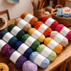 A pile of soft chunky t-shirt yarn in various colors, including orange, pink, green, and purple, laid out on a wooden table.
