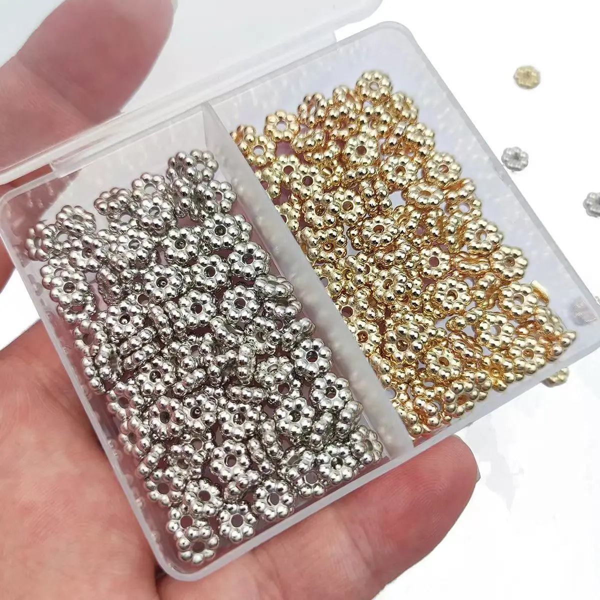 A clear plastic container holds a set of 200 gold and silver snowflake spacer beads for jewelry making.