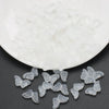 A pile of clear glass butterfly beads for jewelry making on a white dish.