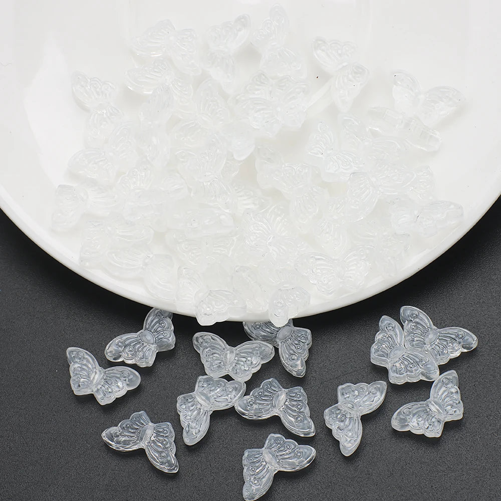 A pile of clear glass butterfly beads for jewelry making on a white dish.