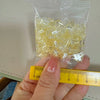 A hand holds a clear plastic bag filled with yellow acrylic ice strips for nail art and DIY crafts next to a ruler.