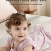 A smiling baby wearing a pink sleeveless sleep sack lying on a light-colored surface.