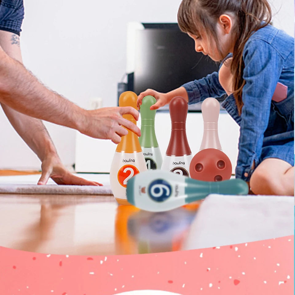 A child is shown interacting with a soft foam bowling set featuring numbers and animal designs on a wooden table.