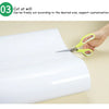 A hand is cutting a white flexible magnetic dry erase board to size with scissors.