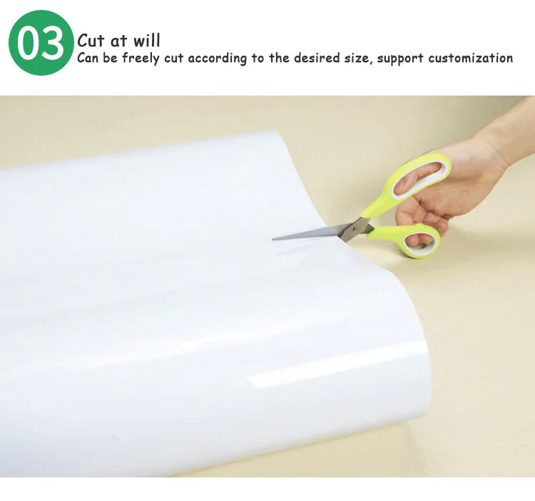 A hand is cutting a white flexible magnetic dry erase board to size with scissors.