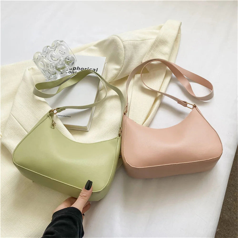 A light green PU square crossbody bag resting on a cream fabric next to a clear glass.
