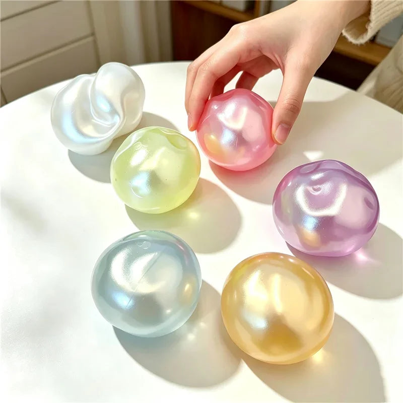 A hand holds several translucent, spherical fidget balls in shades of pink, yellow, and purple on a white surface.