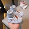A pair of light gray knit bear booties for a baby, shown resting on a hand with other similar items.