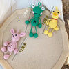 Three handmade crochet frog ornaments in green, yellow, and pink are displayed on a light background.