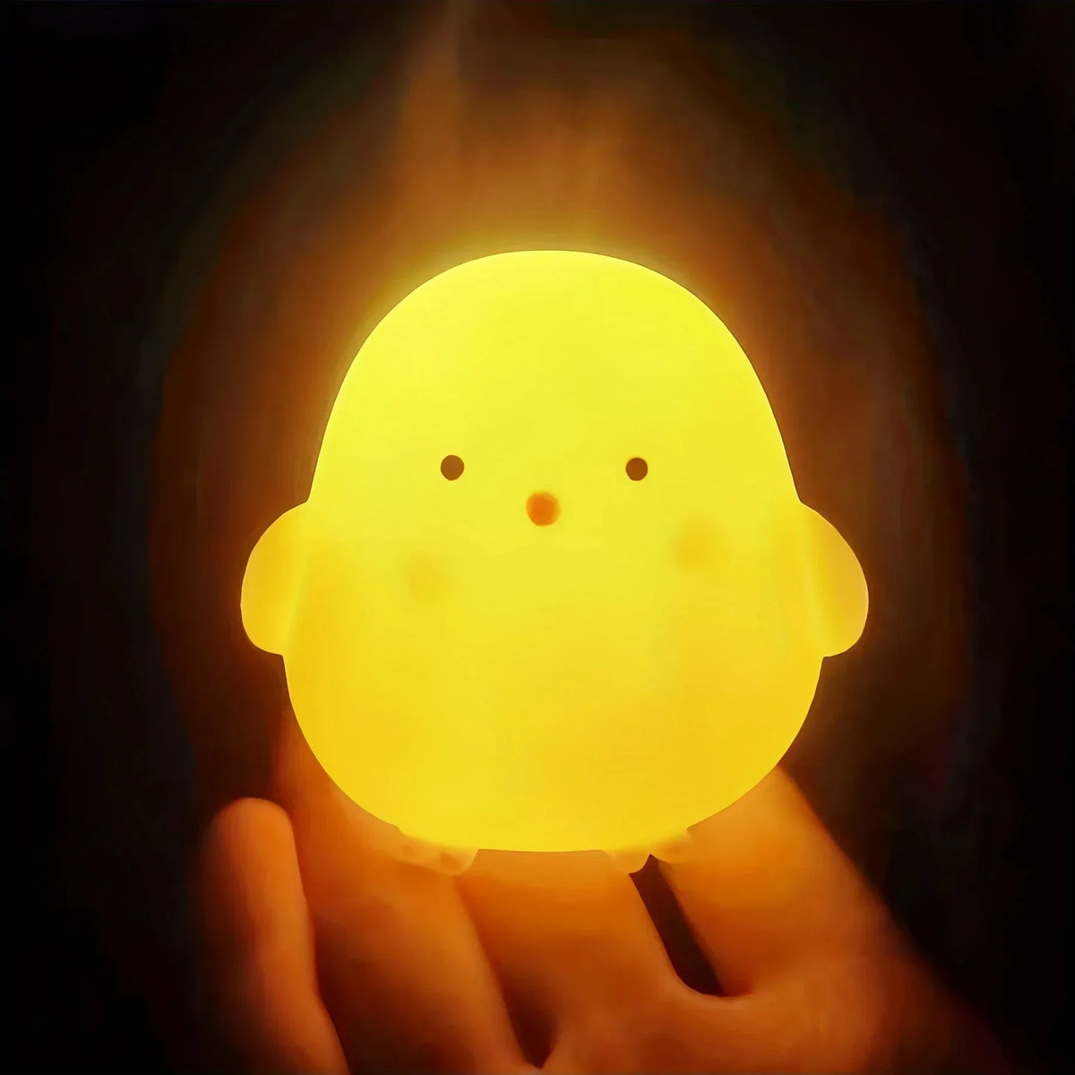 A glowing yellow cartoon duck night light is held in a hand against a dark background.