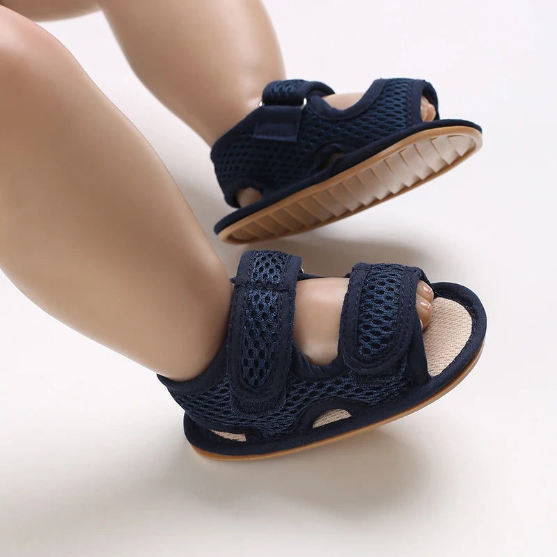 A pair of navy blue breathable first walker sandals for a baby, shown on a child's foot.