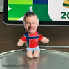A small stuffed doll of Erling Haaland wearing a red and blue football jersey standing on a silver plate.