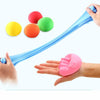 A hand holds a blue modeling clay tube with several colored balls, including yellow, orange, and green.